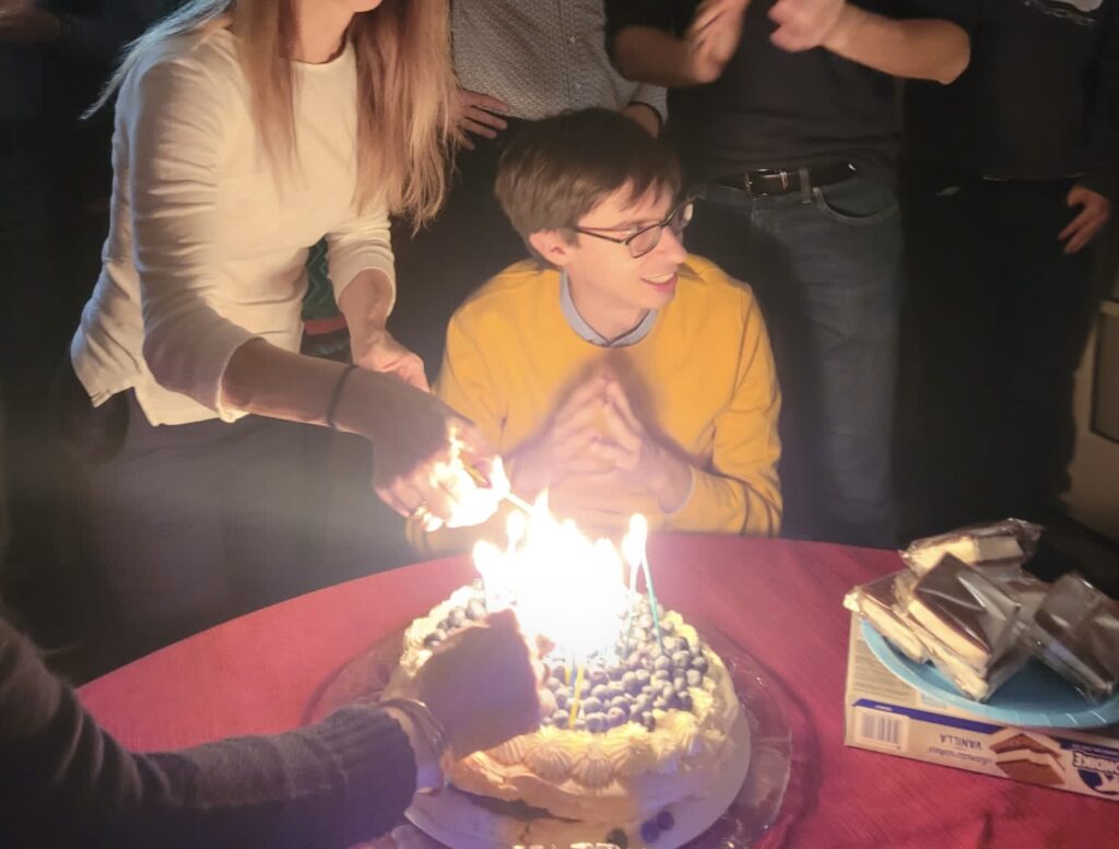 Man in yellow sweater in front of birthday cake