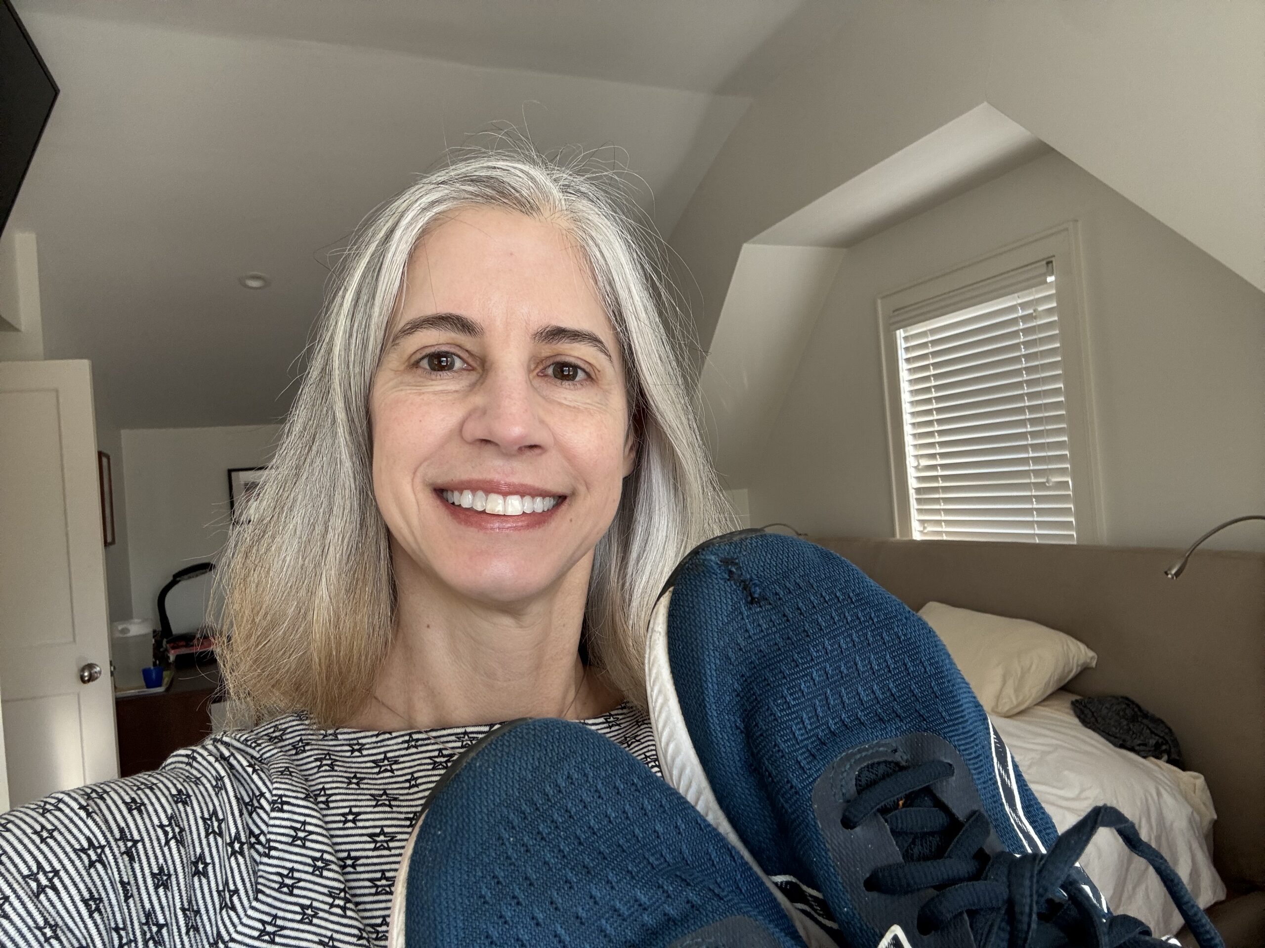 woman smiling and holding up a pair of blue sneakers